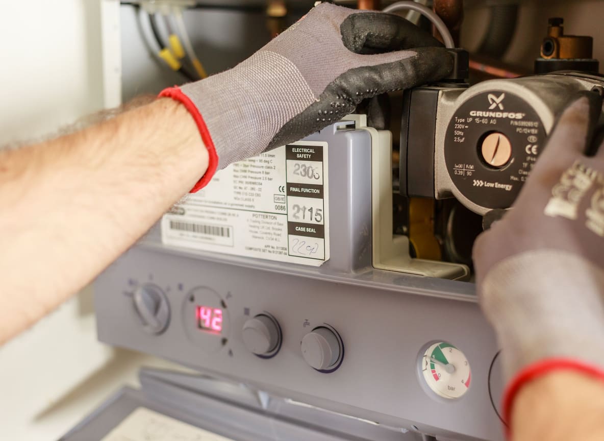 Handen van een technicus met werkhandschoenen die de circulatiepomp van een cv-ketel herstellen