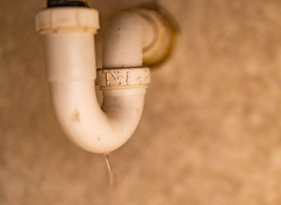 Pvc-sifon onder een wastafel met een druppelend waterlek, typische residentiële loodgieterij